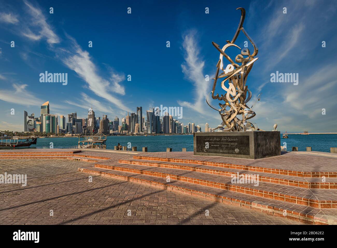 Horizon de Doha Qatar vue lumière du jour avec nuages dans le ciel montrant des gratte-ciel et des charrues en arrière-plan et sculpture de Calligraphie en premier plan Banque D'Images