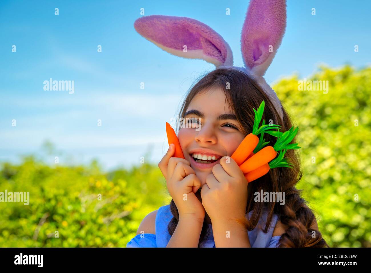 Portrait d'une jolie petite fille de lapin avec des carottes dans les mains appréciant Pâques, ayant un jardinage amusant dans la cour sur une journée ensoleillée de printemps, tenue traditionnelle Banque D'Images