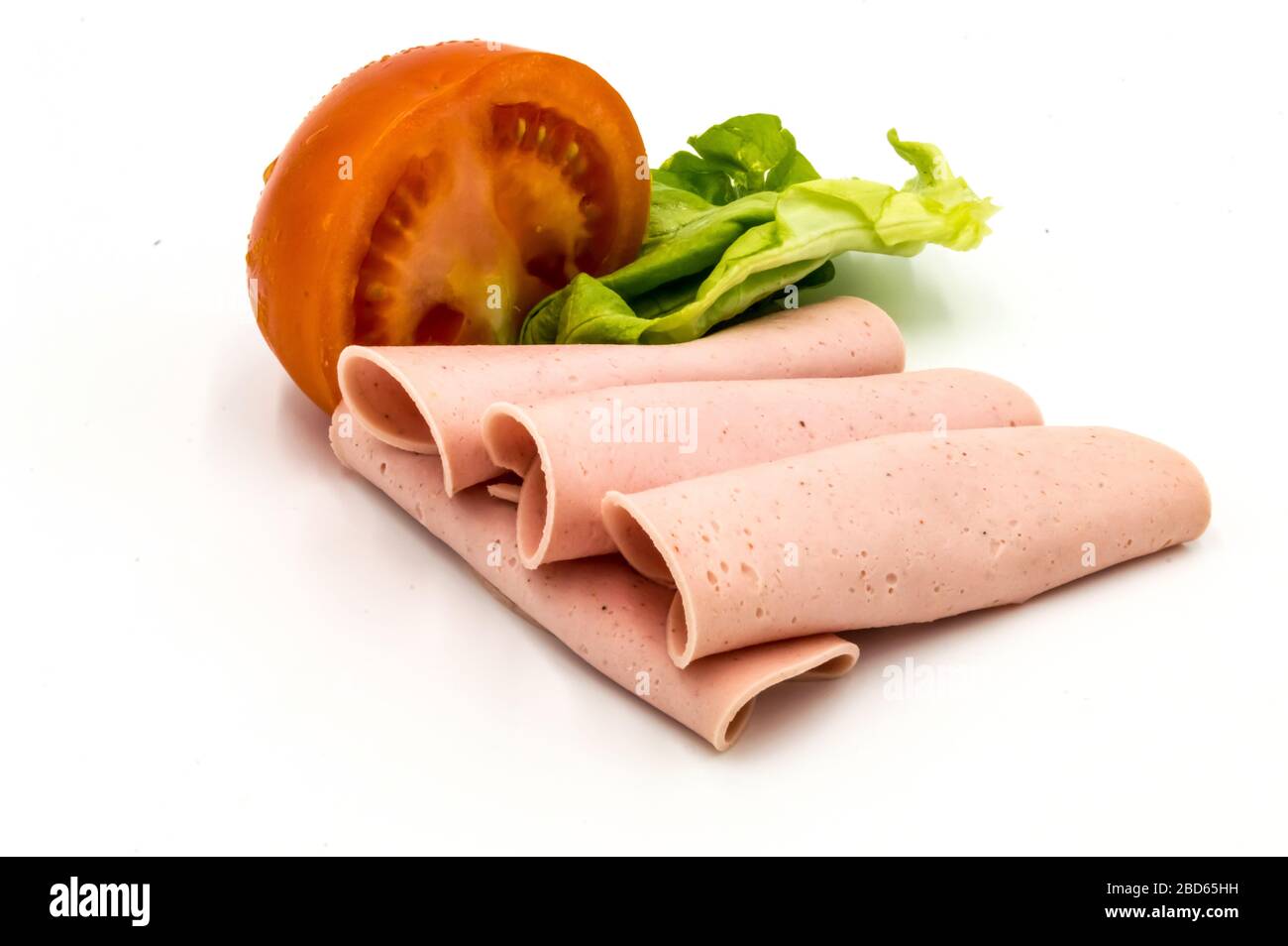 Tranche de jambon ou de saucisse de Paris sur fond blanc avec une demi-tomate et une feuille de salade Banque D'Images