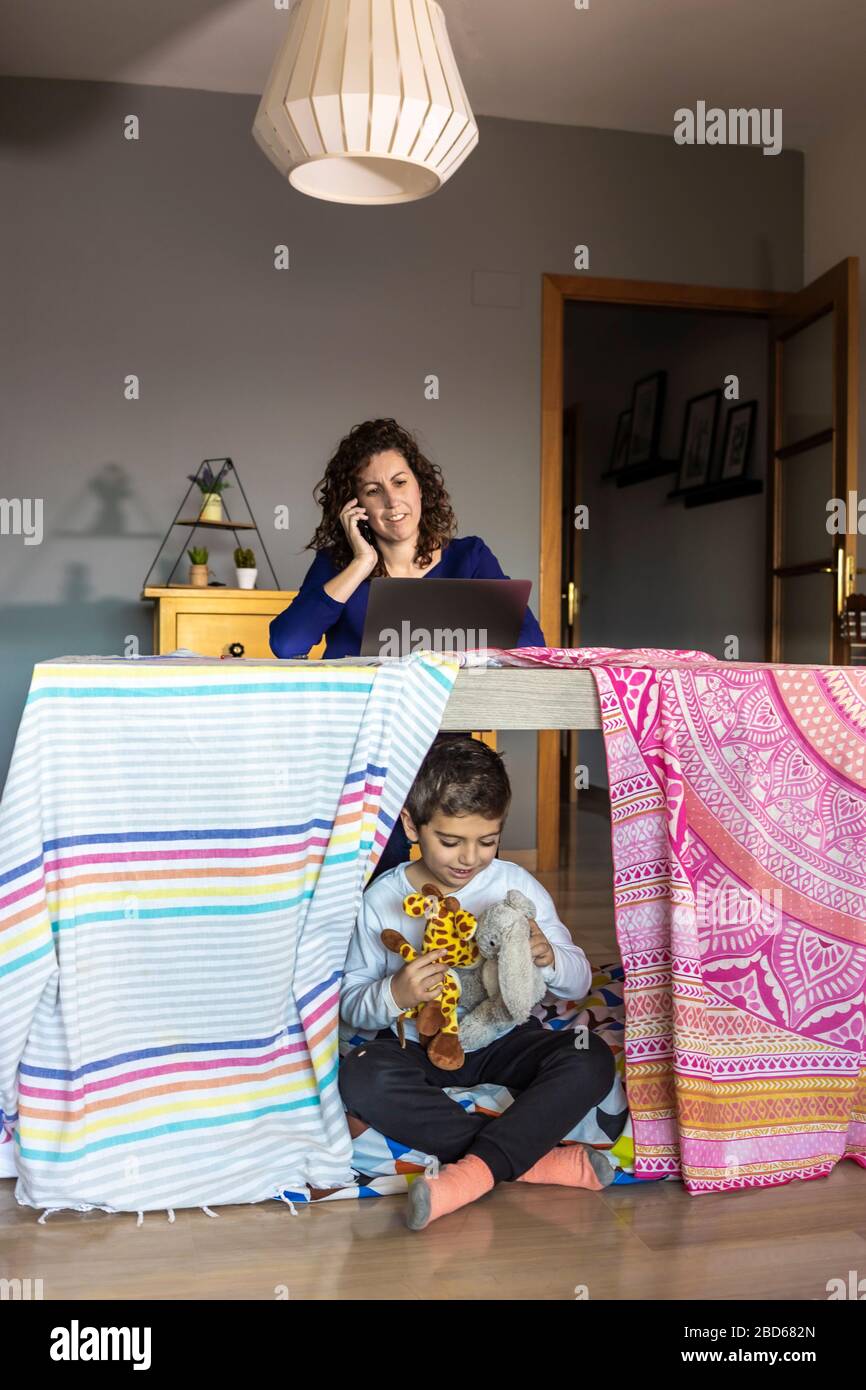 Mère travaillant à la maison pendant que son fils joue Banque D'Images