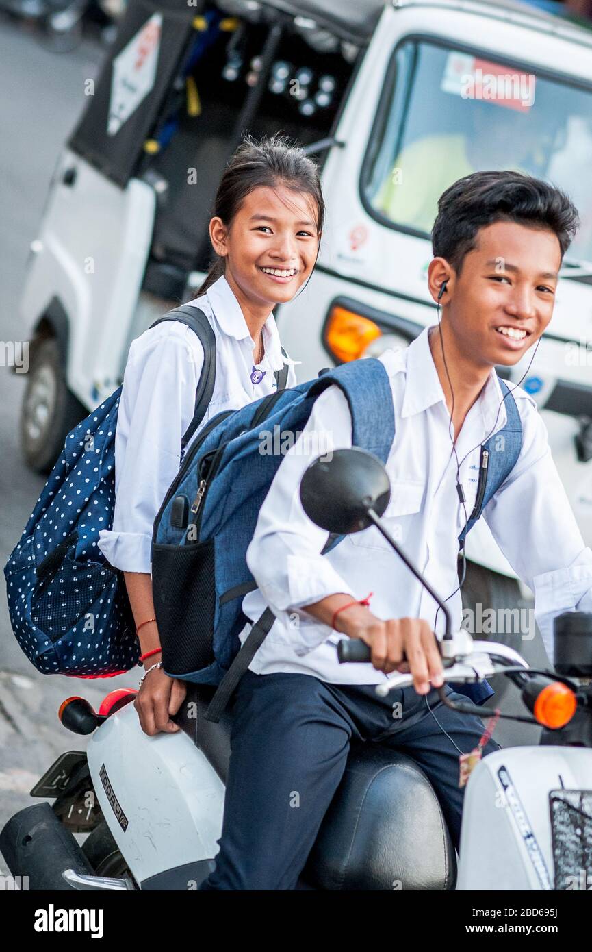 Deux jeunes enfants heureux de l'école naviguent dans les rues animées de Phnom Penh, au Cambodge, sur un scooter. Banque D'Images