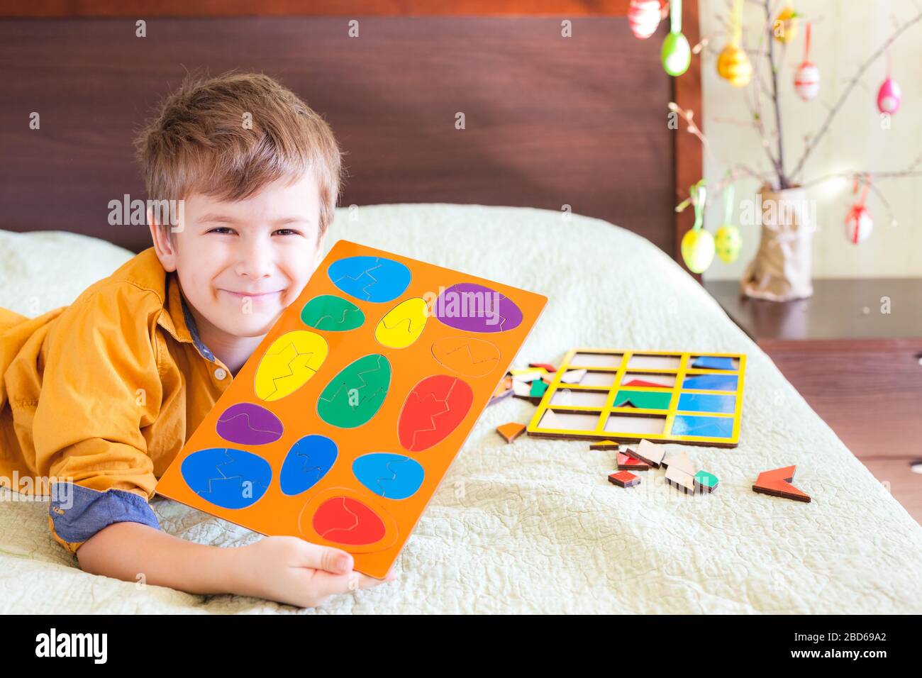 Happy boy montre un puzzle prêt sous la forme d'oeufs de Pâques, intérieur de maison. Décoration de Pâques en arrière-plan Banque D'Images