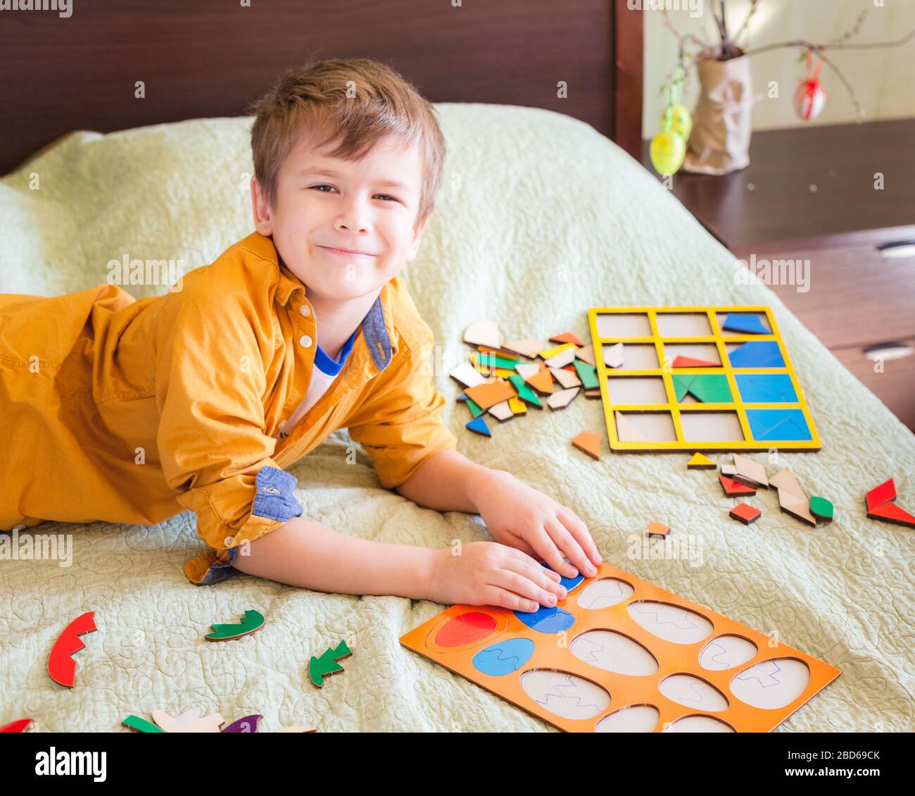 Heureux garçon jouant avec le puzzle en bois sous forme d'oeufs de Pâques, intérieur de maison. Décoration de Pâques en arrière-plan Banque D'Images
