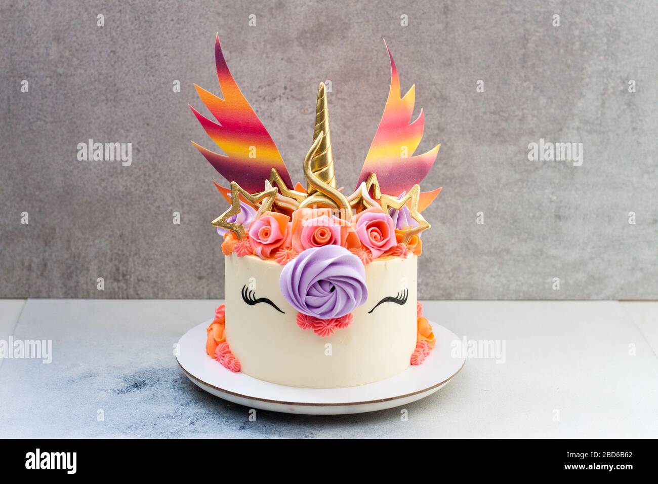 Gâteau unicorn coloré et lumineux avec corne et oreilles dorées, ailes  arc-en-ciel, roses et décor crème fouettée. Fond gris Photo Stock - Alamy