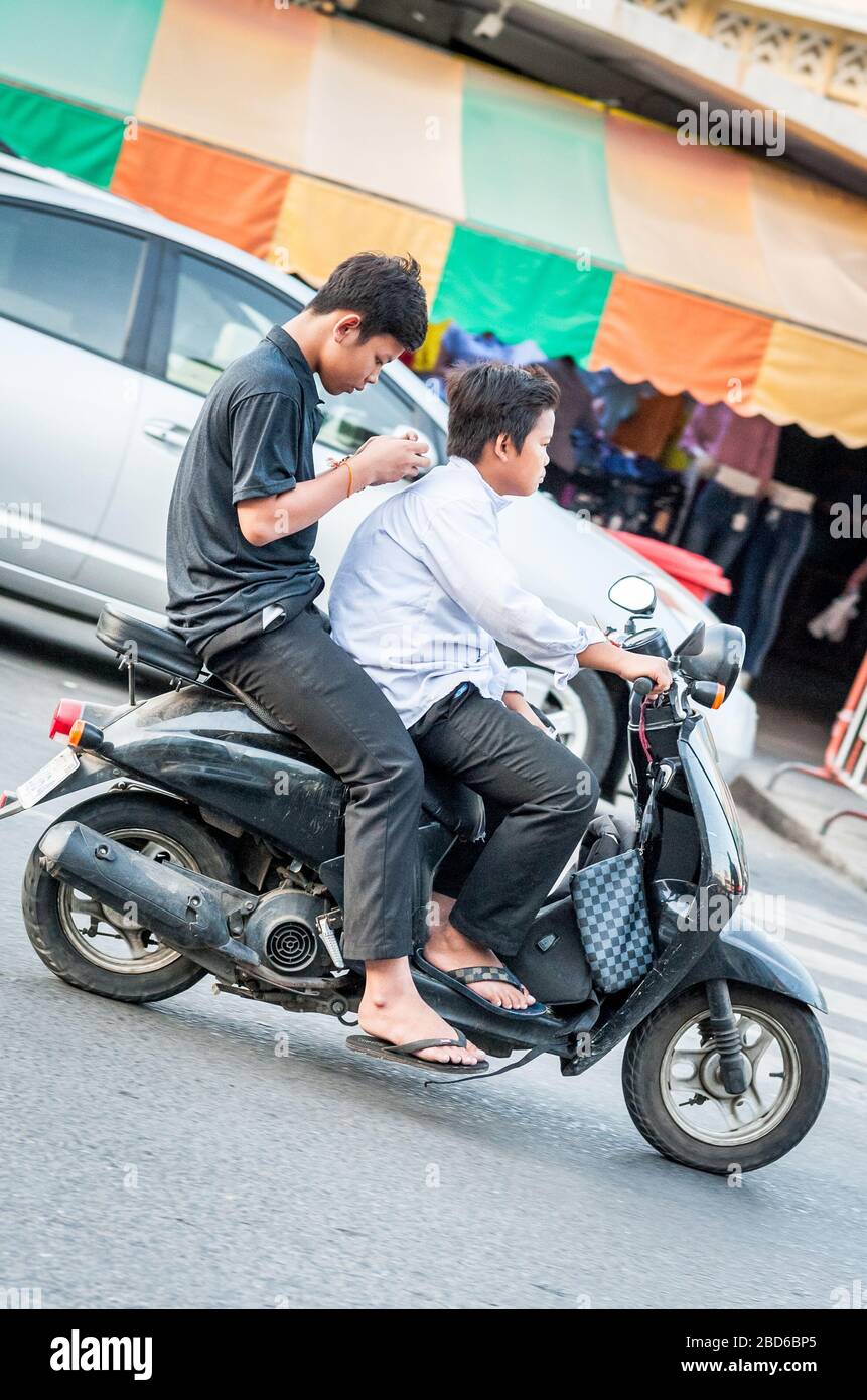 Deux jeunes étudiants cambodgiens se précipitent dans les rues animées de Phnom Penh avec le passager concentré sur son téléphone portable. Banque D'Images