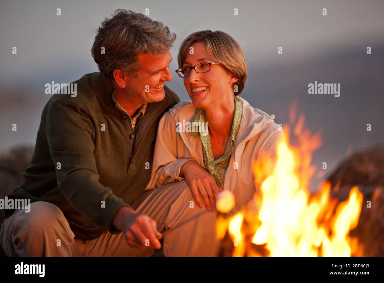 Smiling woman sitting par un feu sur une plage. Banque D'Images