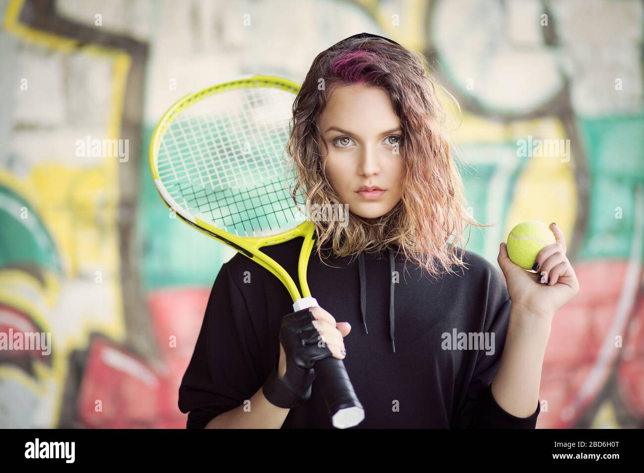 Joli joueur de tennis Teenage regardant votre appareil photo tenant la raquette de tennis et le ballon plein air graffiti arrière-plan Banque D'Images