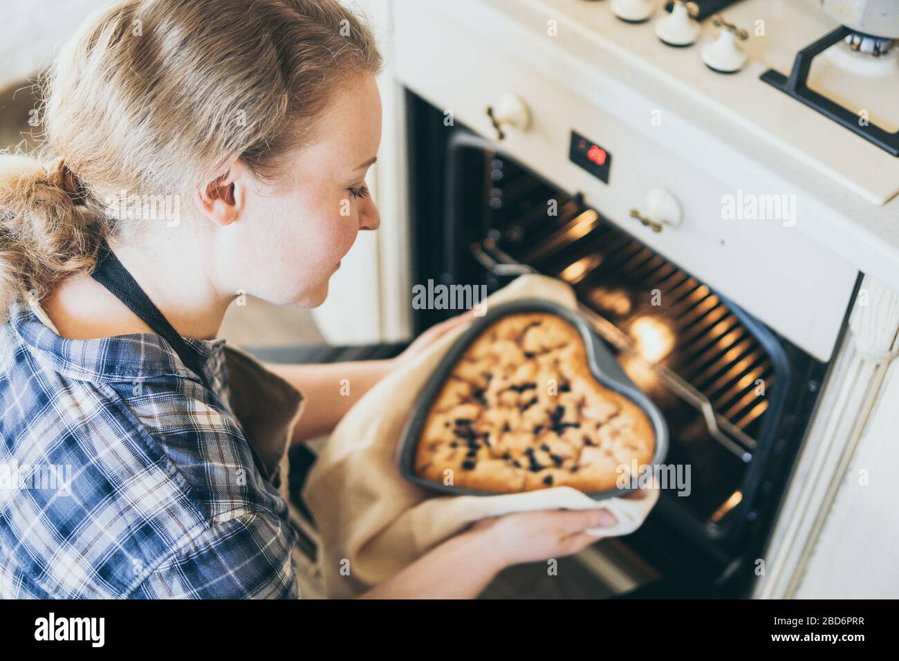 Jeune blonde femme prenant la tarte aux baies en forme de coeur hors du four. Cuisine à la maison et sourire. Banque D'Images