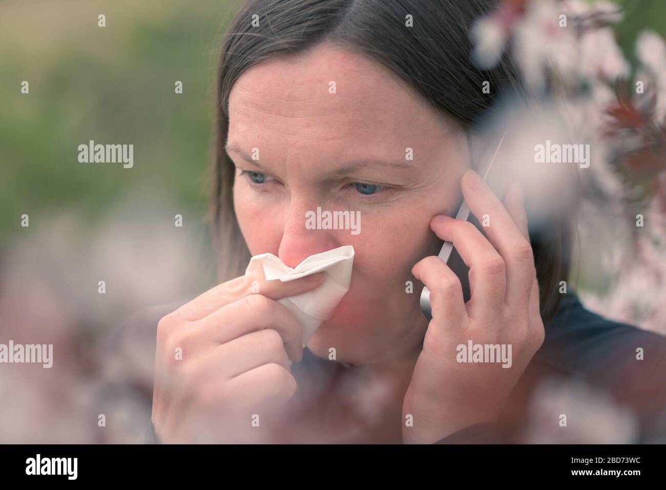 Femme parlant sur téléphone mobile et éternuer, printemps arbre pollen allergie concept Banque D'Images