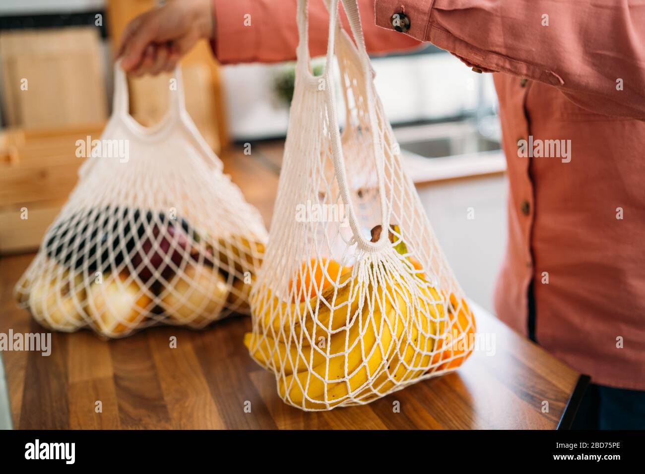 Femme revenez à la maison après avoir fait des achats de fruits et légumes avec sac réutilisable coton biologique et sacs en mesh pour faire des achats. Zéro déchet, sans plastique con Banque D'Images