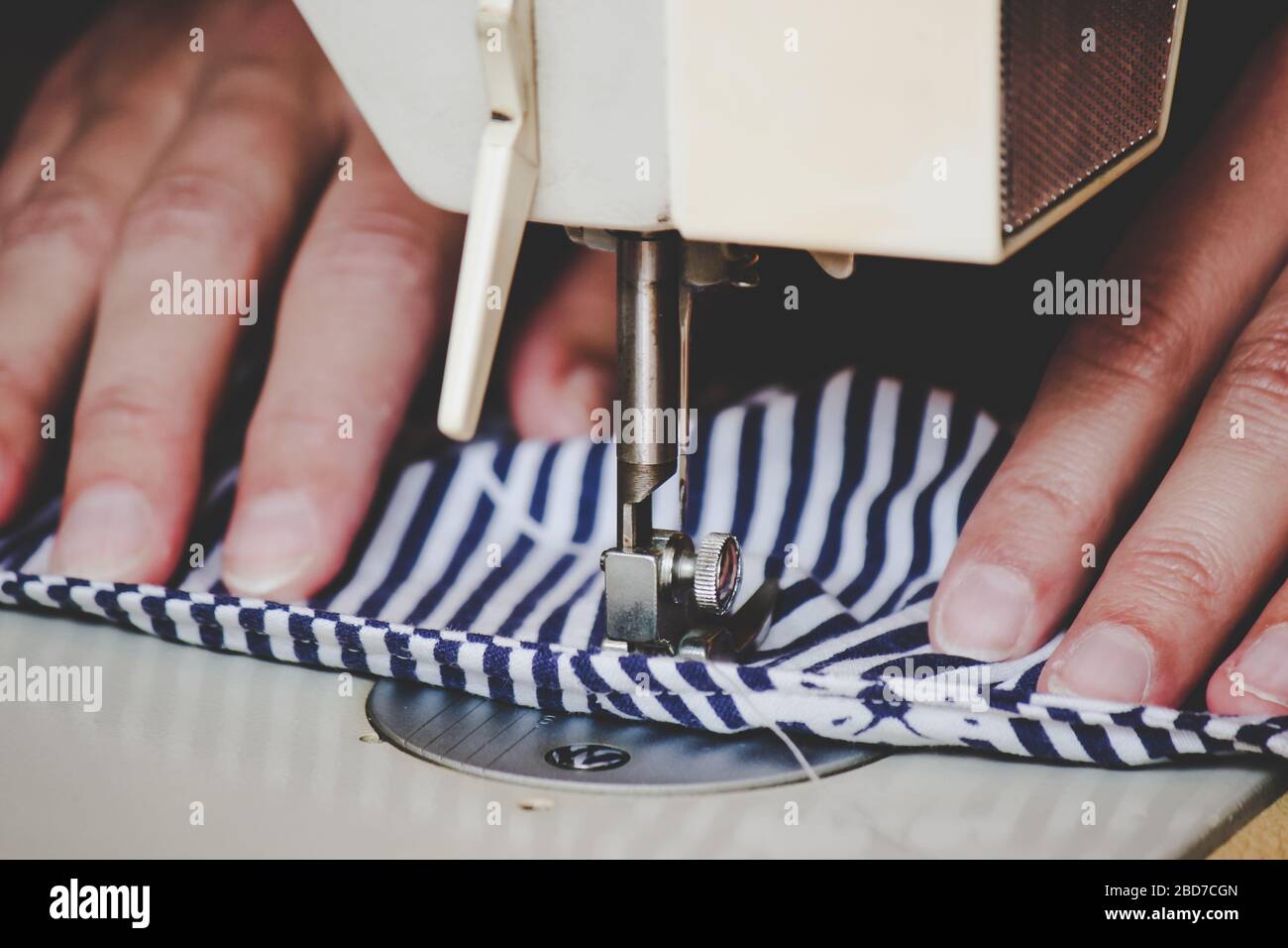 Les mains des femmes utilisant la machine à coudre pour coudre un masque médical coloré du visage pendant la pandémie de coronavirus. Masque de protection fait maison contre le virus. Masques à coudre, COVID-19. Mise au point sélective. Banque D'Images