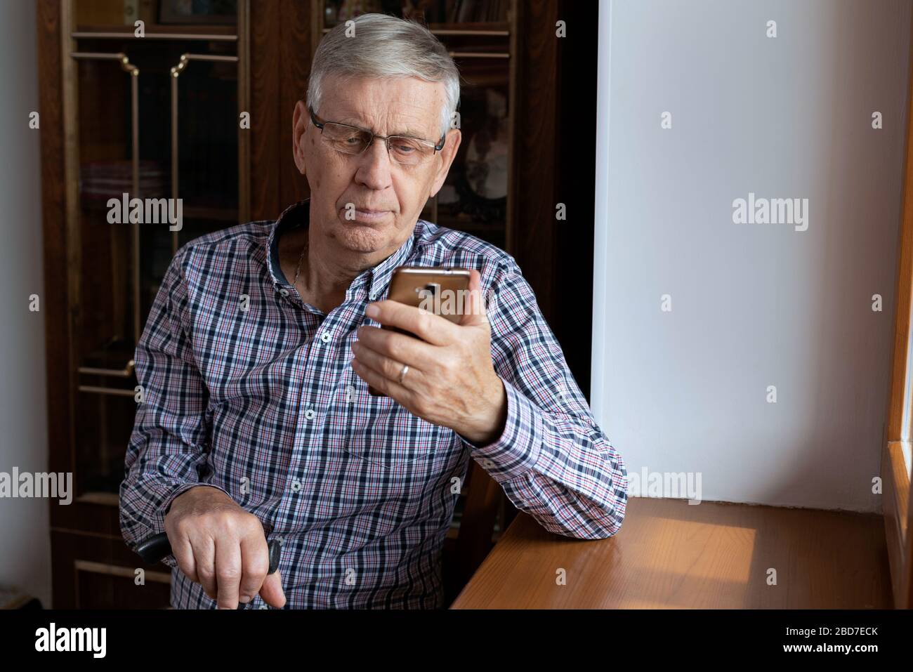 Un homme âgé de 80 ans, assis à la maison, regardant le smartphone. Banque D'Images