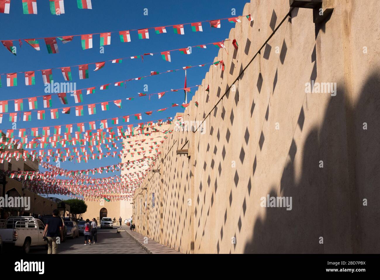 Omanis passe un mur avec les ombres des drapeaux laissant des motifs sur sa façade à Nizwa Souk, Nizwa, Oman Banque D'Images