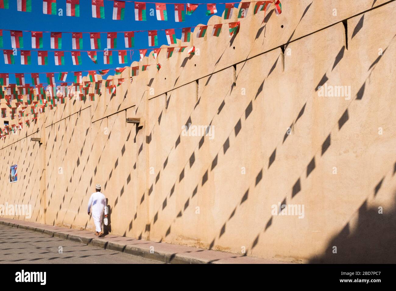 Omanis passe un mur avec les ombres des drapeaux laissant des motifs sur sa façade à Nizwa Souk, Nizwa, Oman Banque D'Images