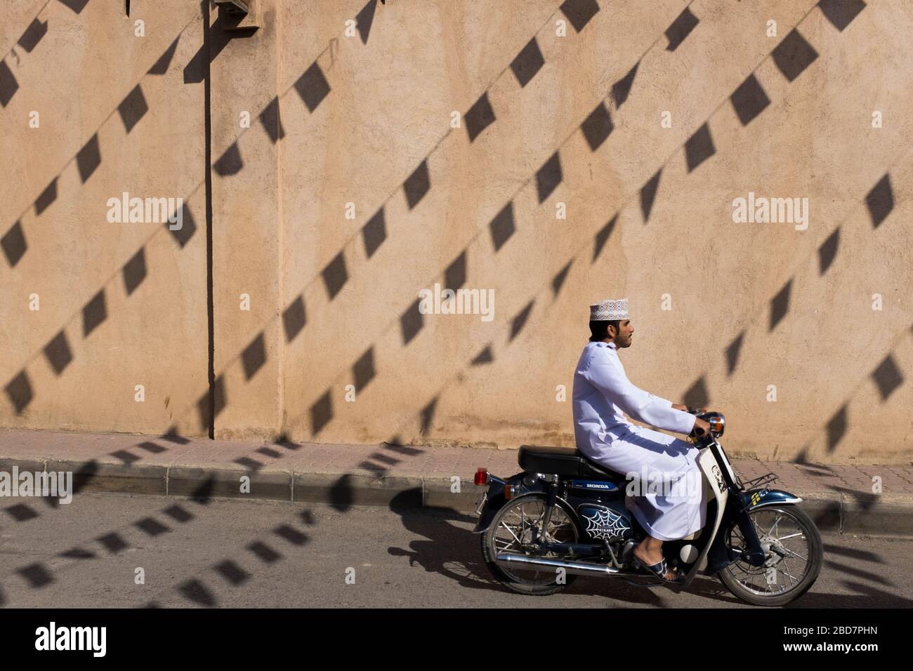 Omanis passe un mur avec les ombres des drapeaux laissant des motifs sur sa façade à Nizwa Souk, Nizwa, Oman Banque D'Images