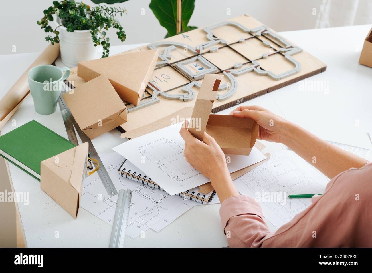 Box Maker travaillant derrière une table, repliant, façonnant une boîte, outils dispersés à travers Banque D'Images