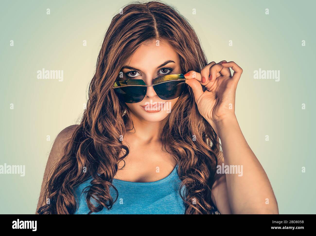 Headshot sérieuse femme sorceuse en colère tenant des lunettes de soleil vers le bas sceptique regardant vous isolé vert jaune mur fond, chemise bleue. Humain f Banque D'Images
