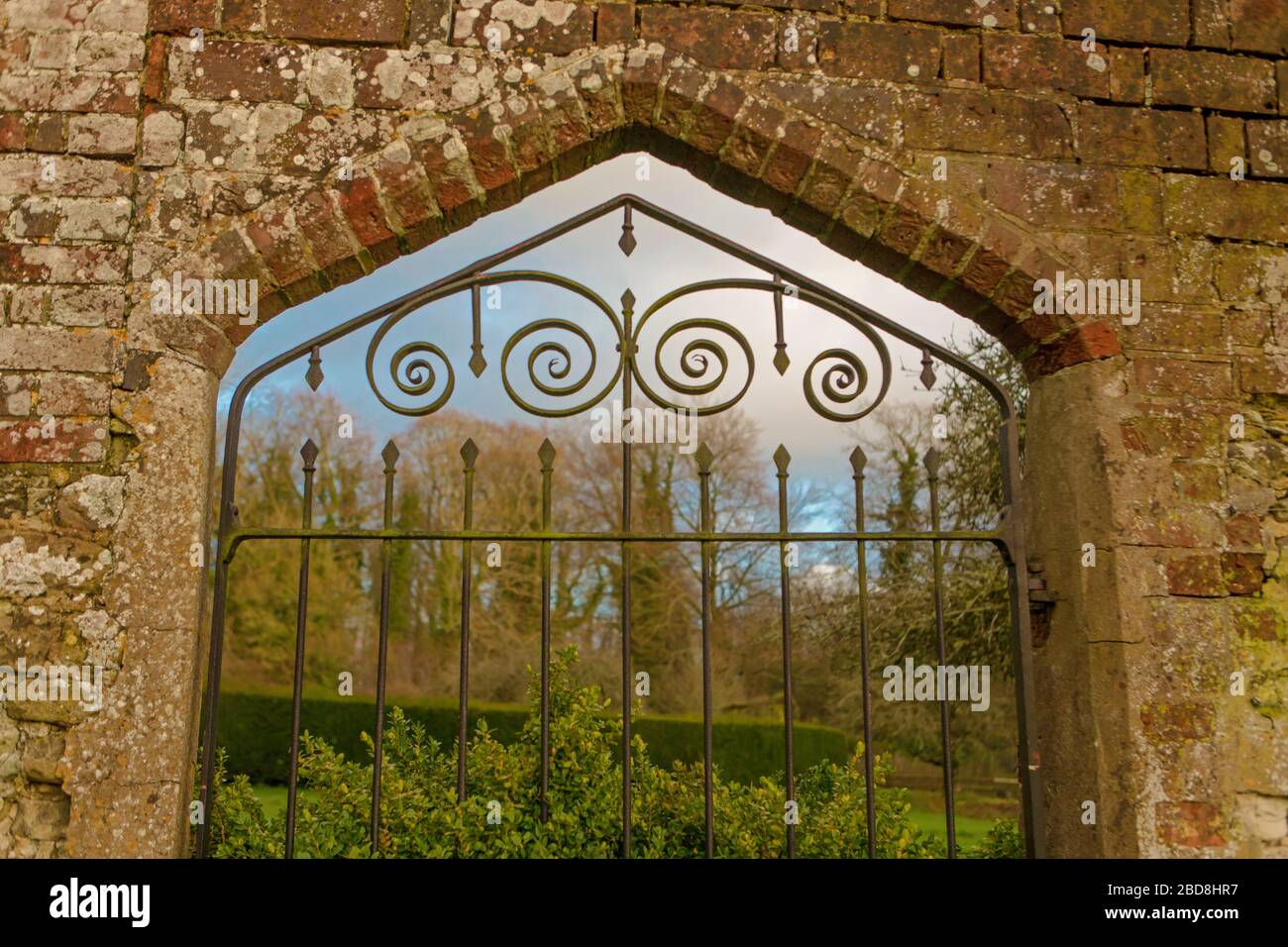 Entrée de la porte en fer forgé au jardin clos avec bois dans le jardin de  Chawton House montrant des briques et des pierres dans la construction de  mur Photo Stock -