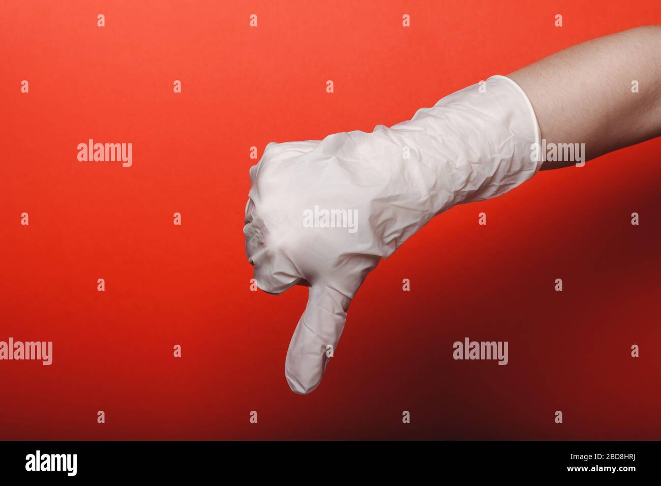 La main d'enfant dans le grand gant médical montre le pouce vers le bas sur fond rouge, place pour le texte Banque D'Images