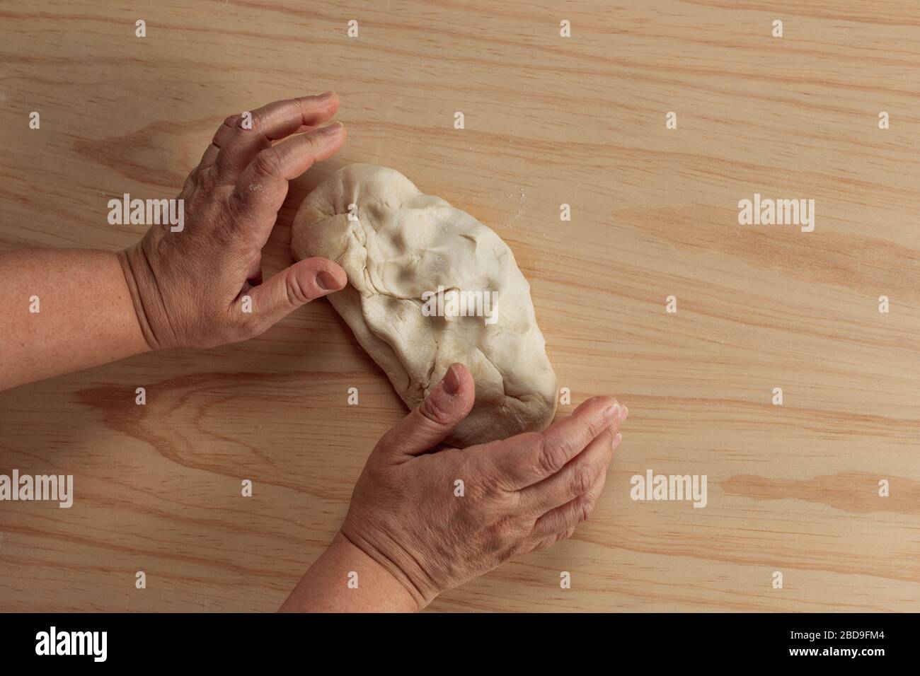 Vue en hauteur des mains d'une femme adulte pétrir la pâte à pizza dans une table en bois de la cuisine Banque D'Images
