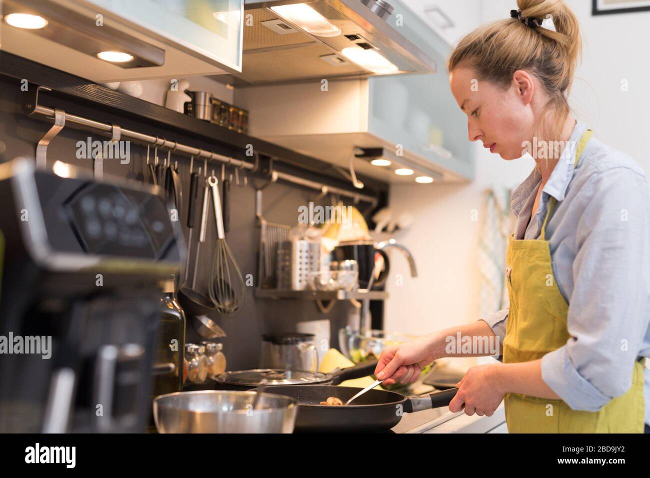 Restez chez la femme au foyer en cuisine, en sautant dans une casserole, en préparant la nourriture pour le dîner en famille. Banque D'Images