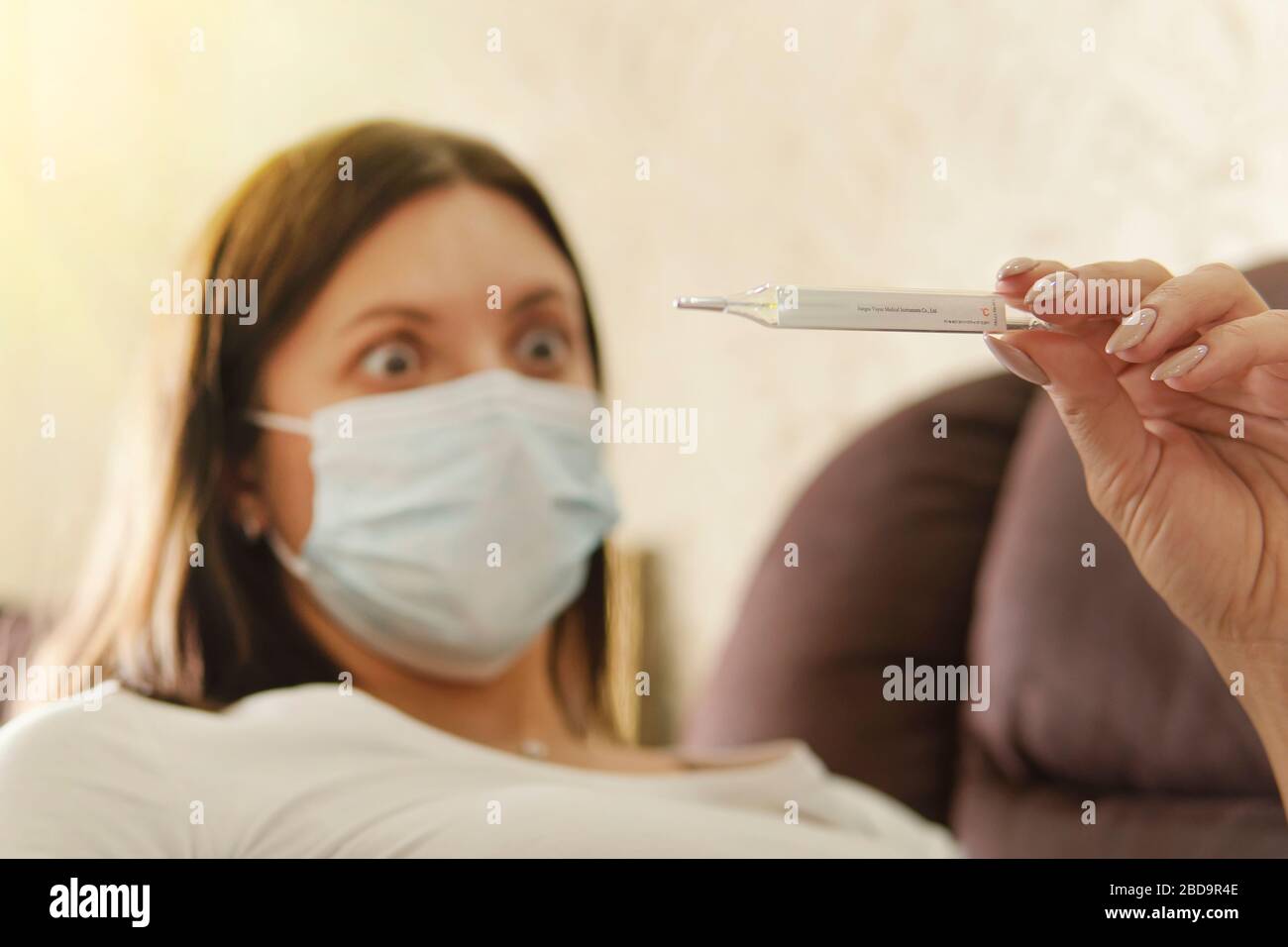 Fille dans un masque d'un virus avec thermomètre dans les mains. Épidémie de coronovirus. Température, thermomètre. Femme est surpris par la température élevée sur therm Banque D'Images