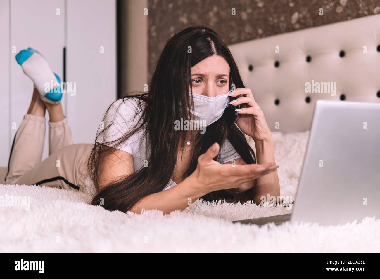Fille dans un masque travaille sur un ordinateur portable à la maison en isolement. Fille masquée travaille sur un ordinateur portable à la maison en quarantaine. Travailler sur l'accès à distance. Auto-isolation Banque D'Images