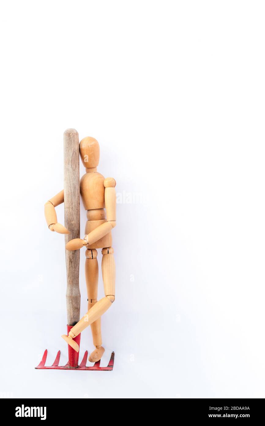 Un homme en bois a graé un râteau rouge sur un fond clair. Disposition verticale. Banque D'Images