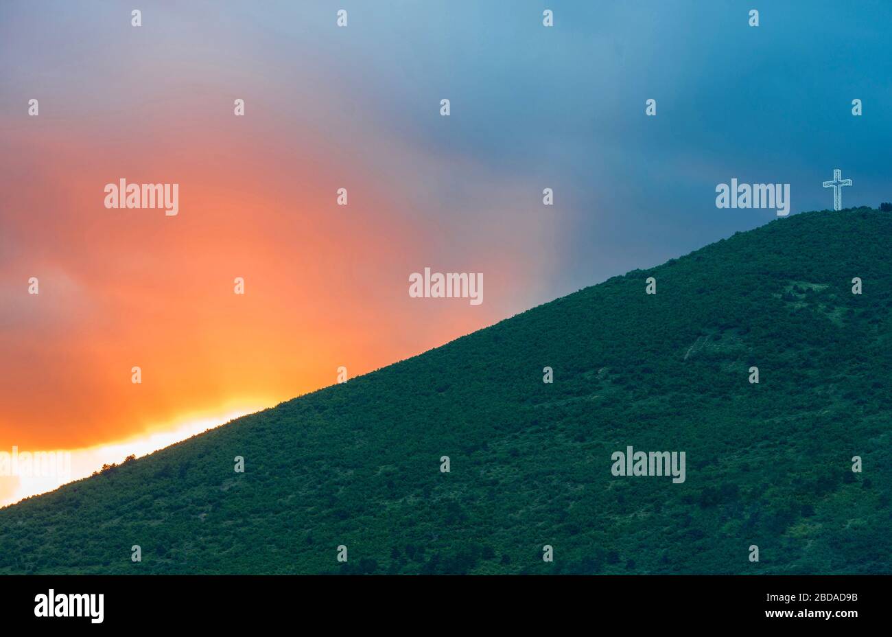 Coucher de soleil dans le ciel derrière une colline verte. Une statue de croix sur le sommet de la colline. Banque D'Images