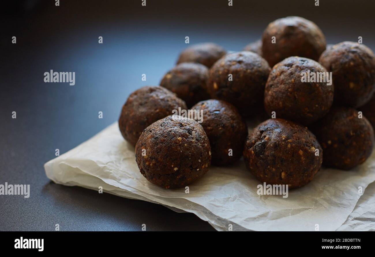 Boules d'énergie sur papier de cire cuit sur un fond noir. Produit vegan brut fait à la main. Ne faites pas cuire. Gros plan. Banque D'Images