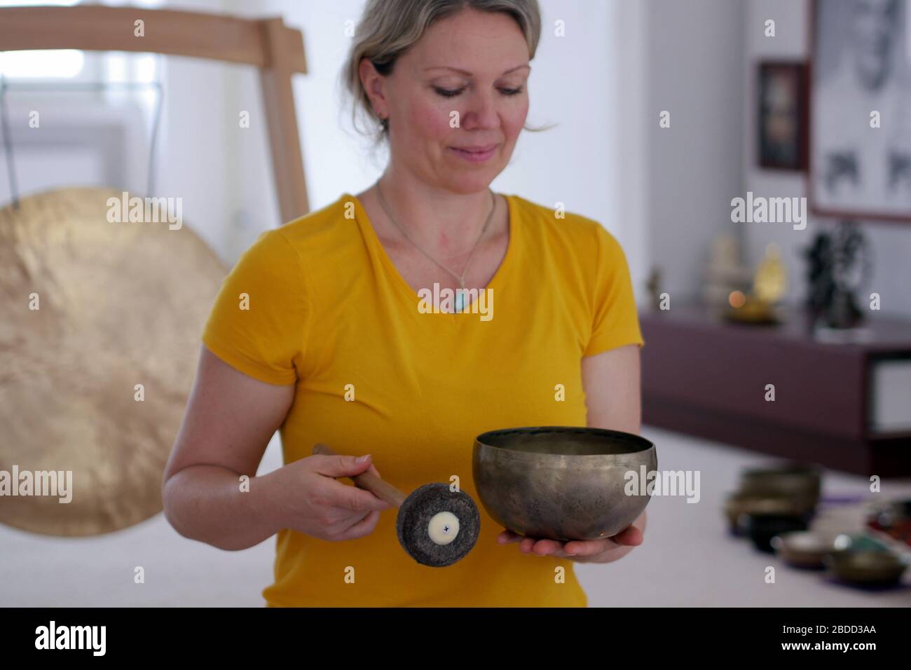 Gros plan sur une femme dans un tee-shirt jaune jouant au bol de chant tibétain. Banque D'Images