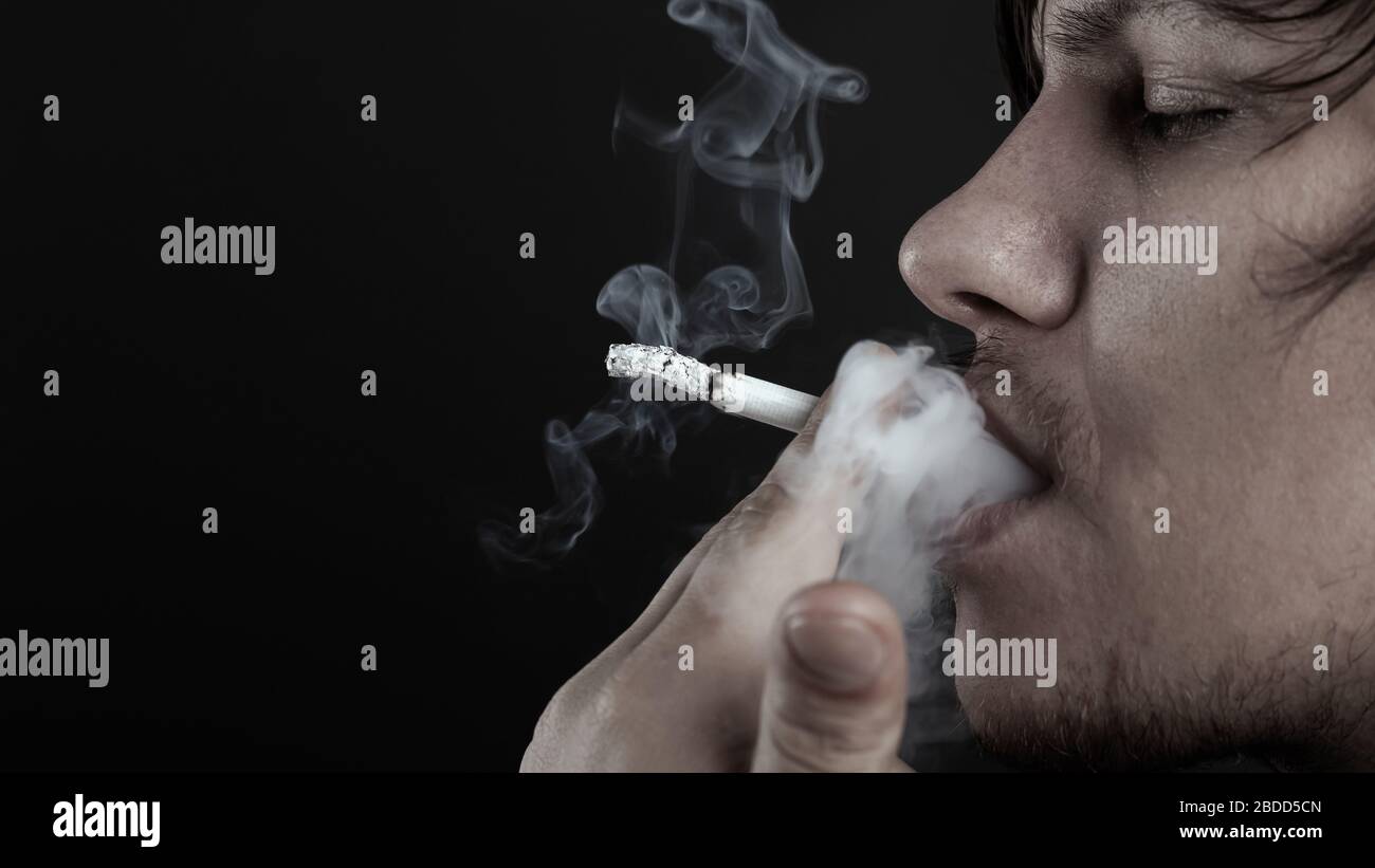 l'homme fume une cigarette sur fond sombre. personne déprimée. Banque D'Images