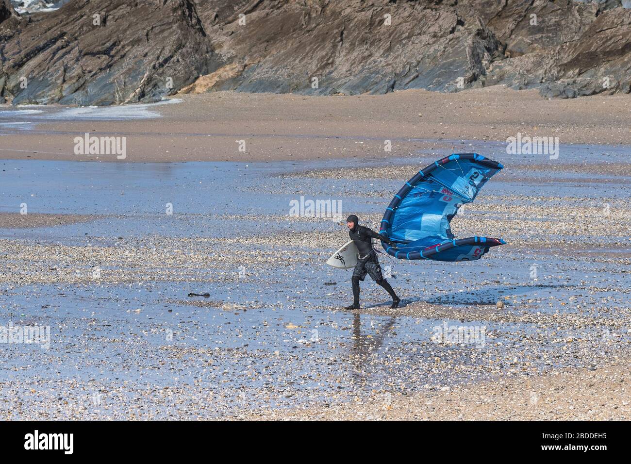 Un surfeur de kite-boarder qui a du mal à transporter son équipement de kite-board dans les vents forts sur la plage de Fistral à Newquay, dans les Cornouailles. Banque D'Images