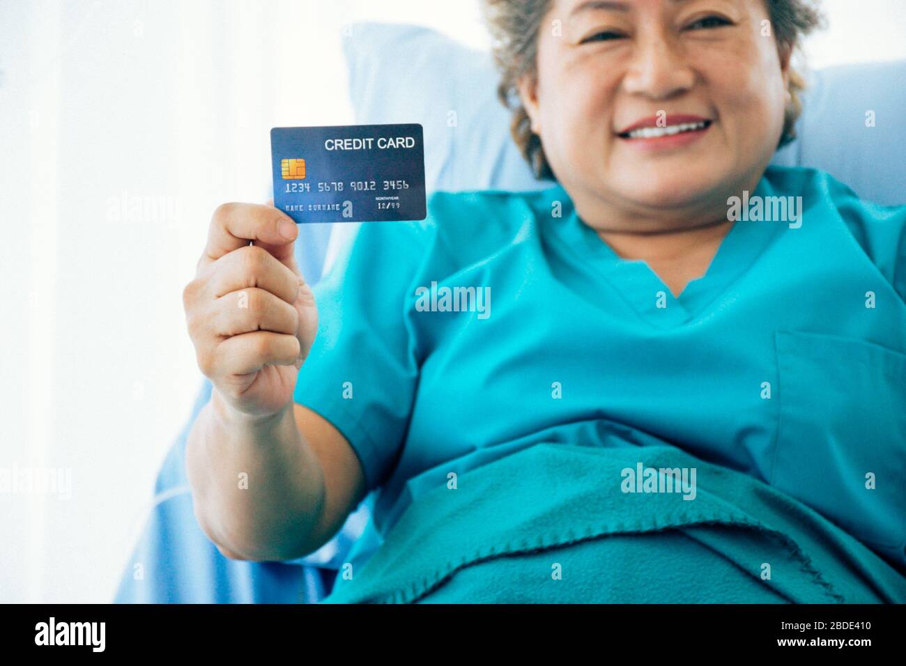 Une femme asiatique âgée montre une carte de santé/carte de crédit moqueuse alors qu'elle est allongé dans le lit à l'hôpital, foyer sélectif Banque D'Images