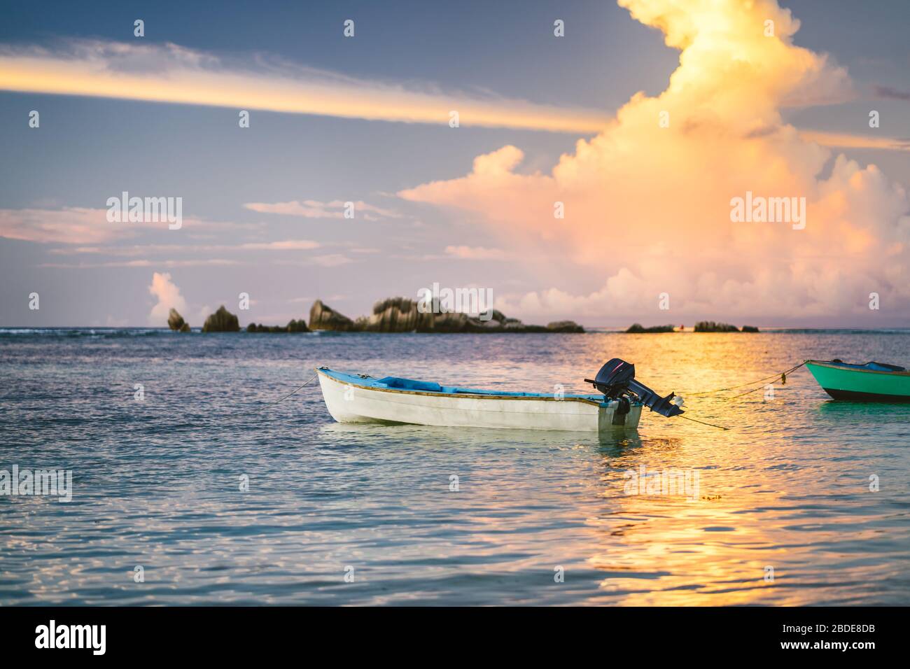 Nuages dorés violets éclairés par le coucher du soleil sur la Digue. Un bateau de pêche flotte dans la baie de l'océan avec des couleurs de feu à l'horizon Banque D'Images