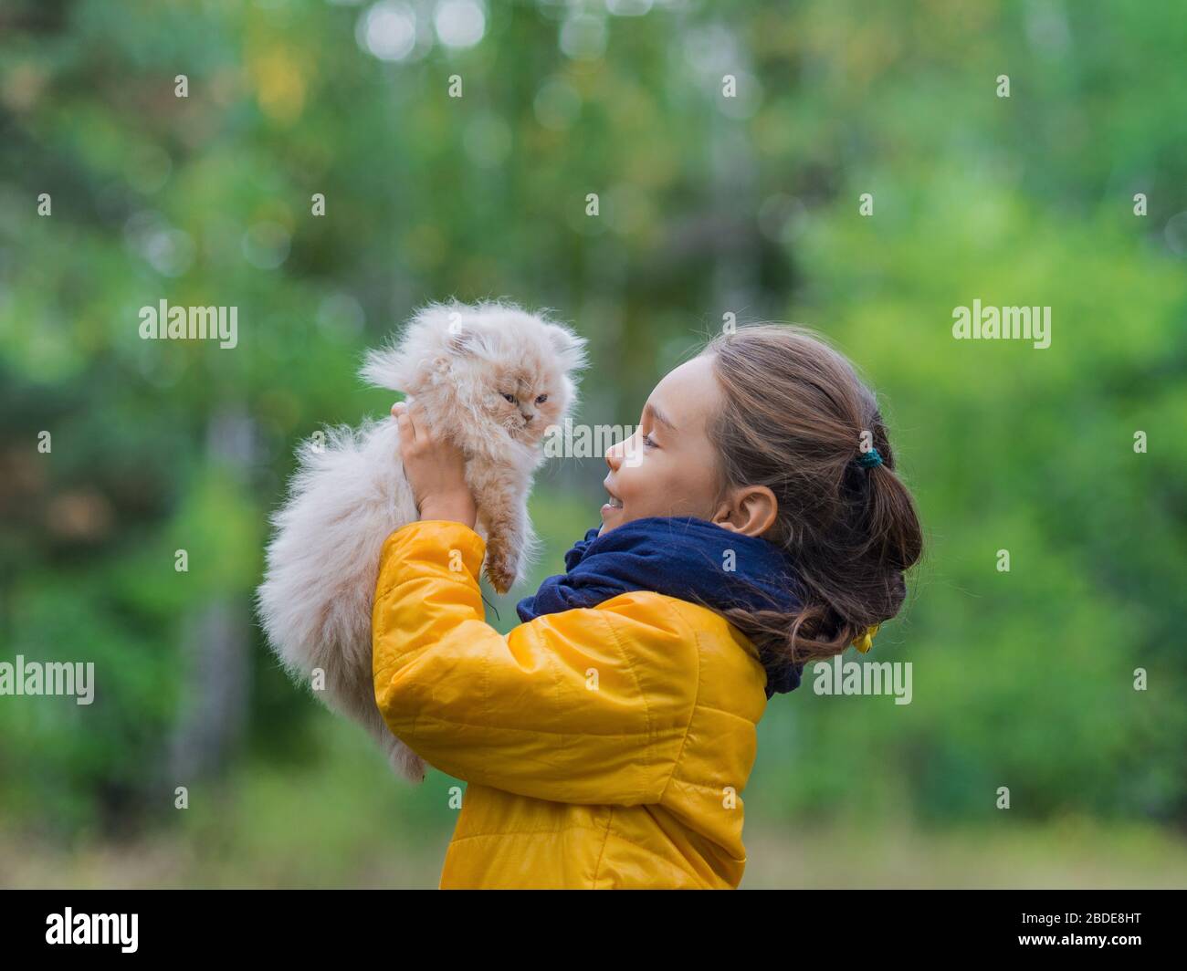 Petite fille sourieuse avec chat sur fond naturel. Concept d'animaux de compagnie. Banque D'Images