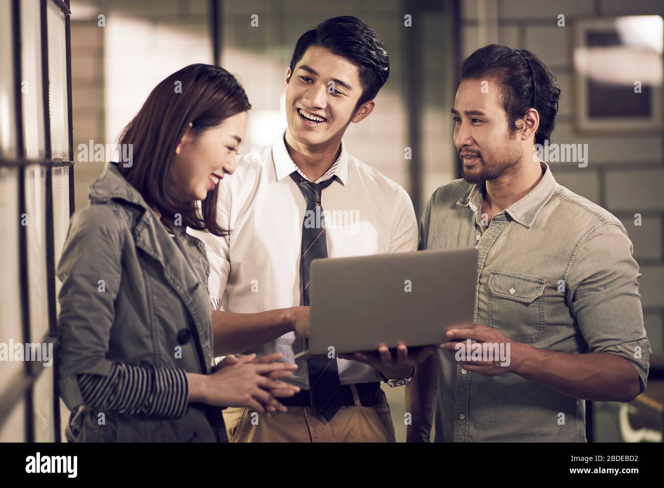 une équipe de trois jeunes entrepreneurs asiatiques d'affaires ayant une discussion utilisant un ordinateur portable au bureau heureux et souriant Banque D'Images