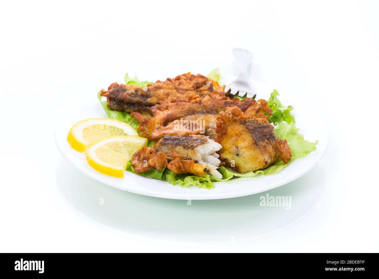 poisson frits hake dans la pâte avec laitue et citron dans une plaque isolée sur fond blanc Banque D'Images