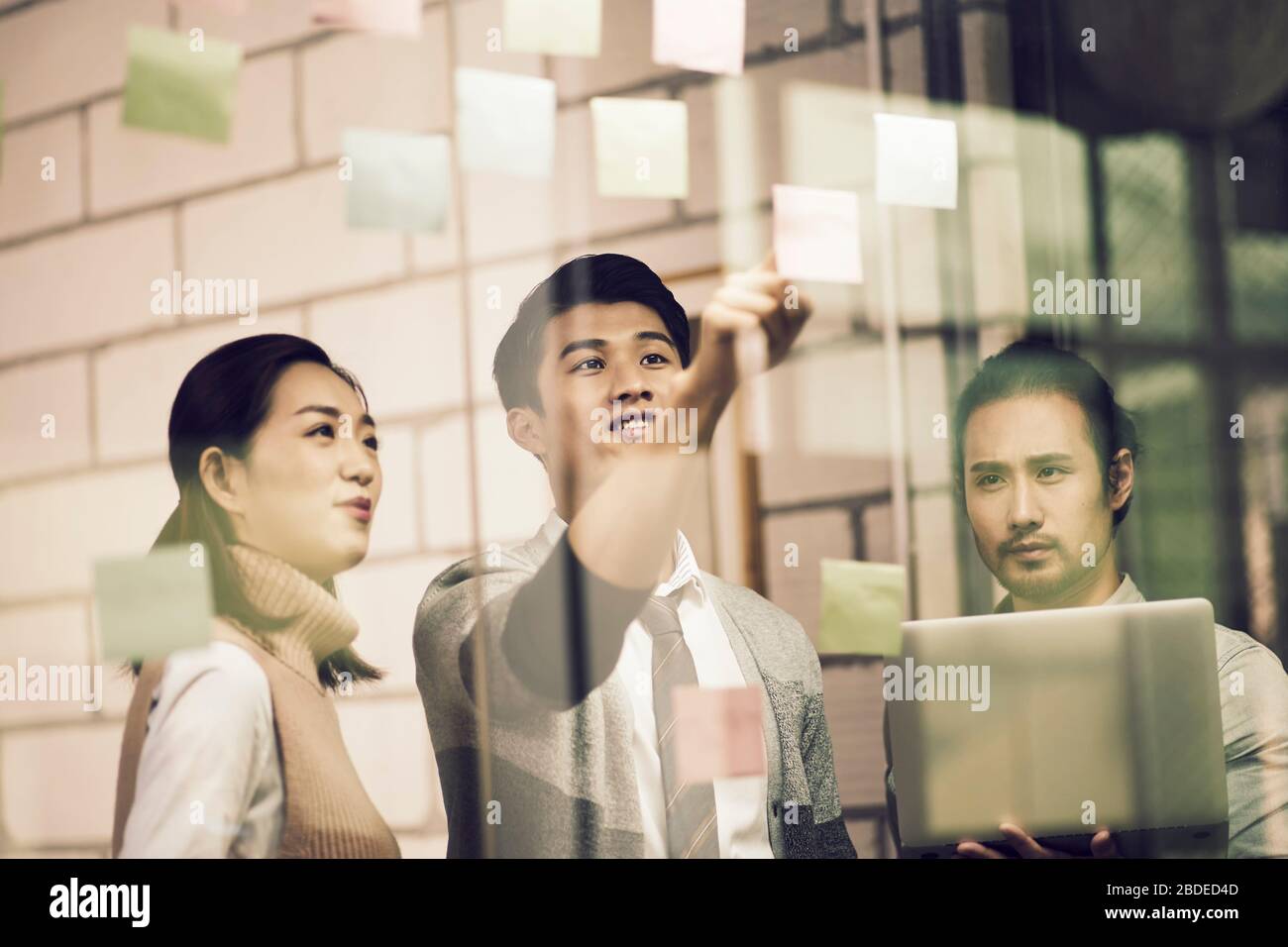 trois jeunes entrepreneurs asiatiques de petite entreprise se moquant de leurs discussions au bureau à l'aide de notes collantes Banque D'Images