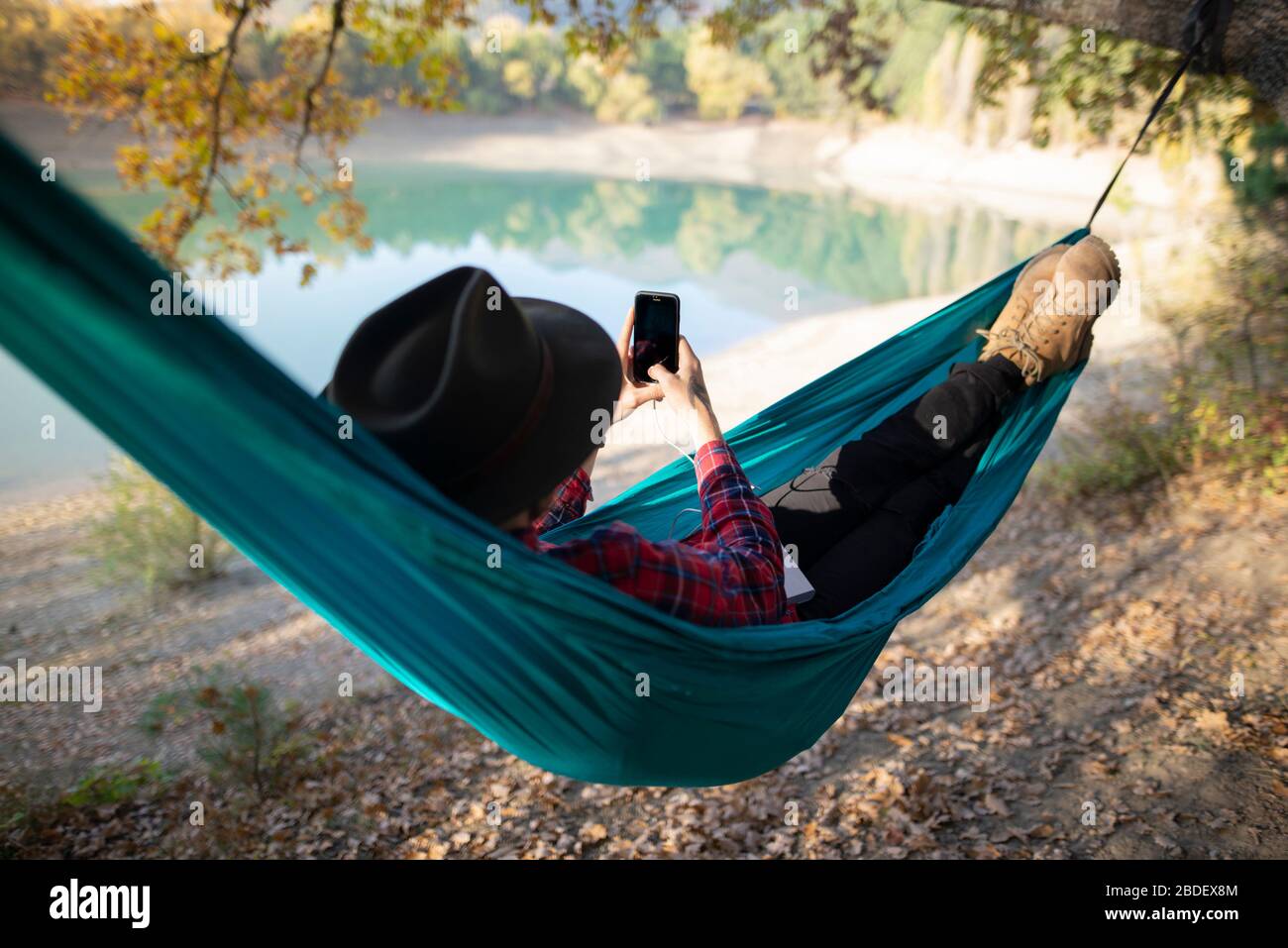 Italie, Homme couché dans un hamac près du lac et utilisant un smartphone Banque D'Images