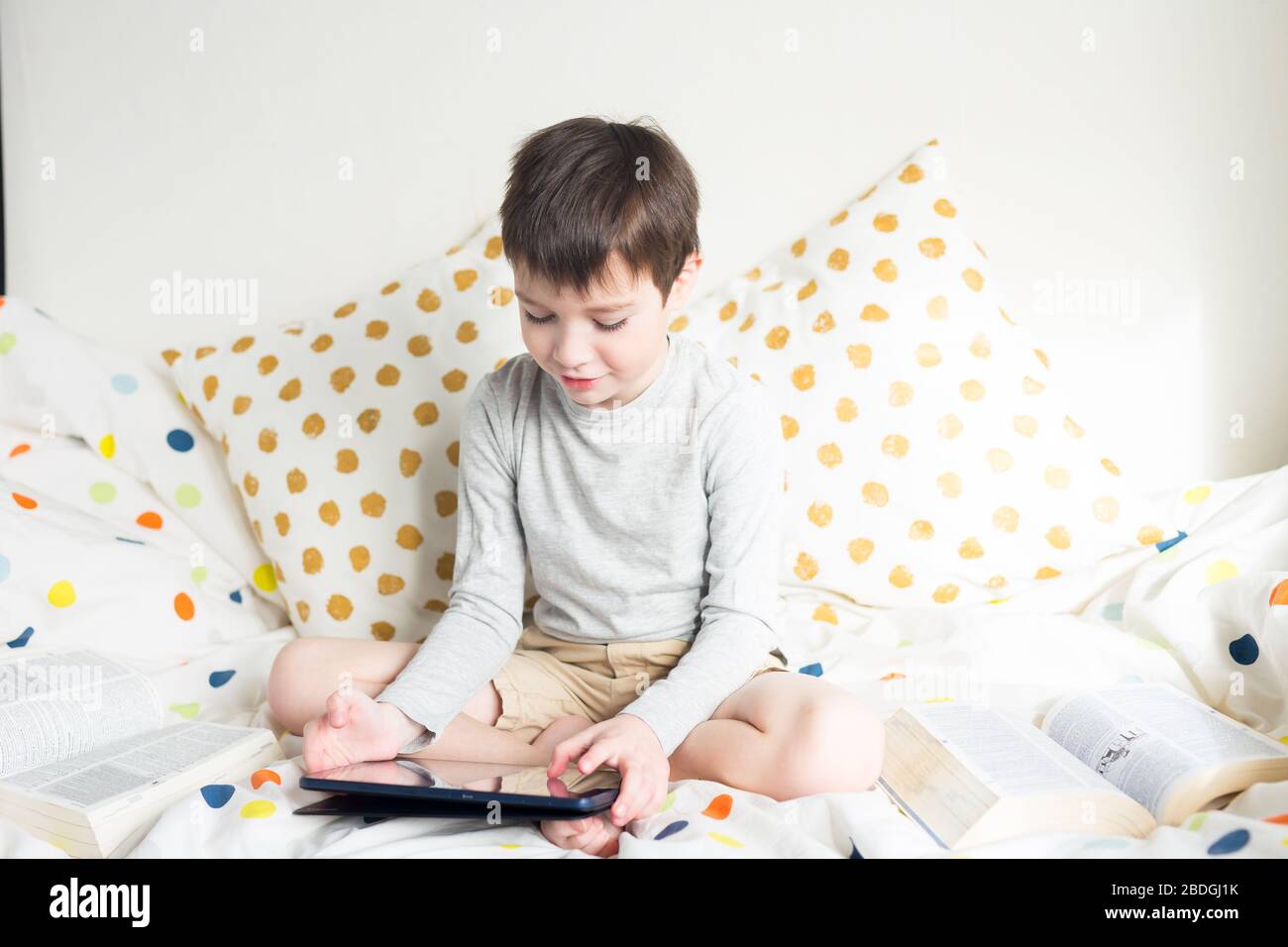 Garçon joue avec smartphone. School Boy sur le lit à la maison avec tablette numérique à la main, faire des devoirs à l'école. Retour à l'école. Formation à distance en ligne educ Banque D'Images