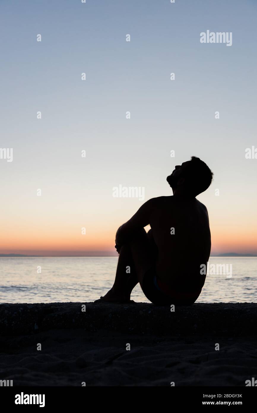 Silhouette d'un homme au bord de la mer au coucher du soleil Banque D'Images