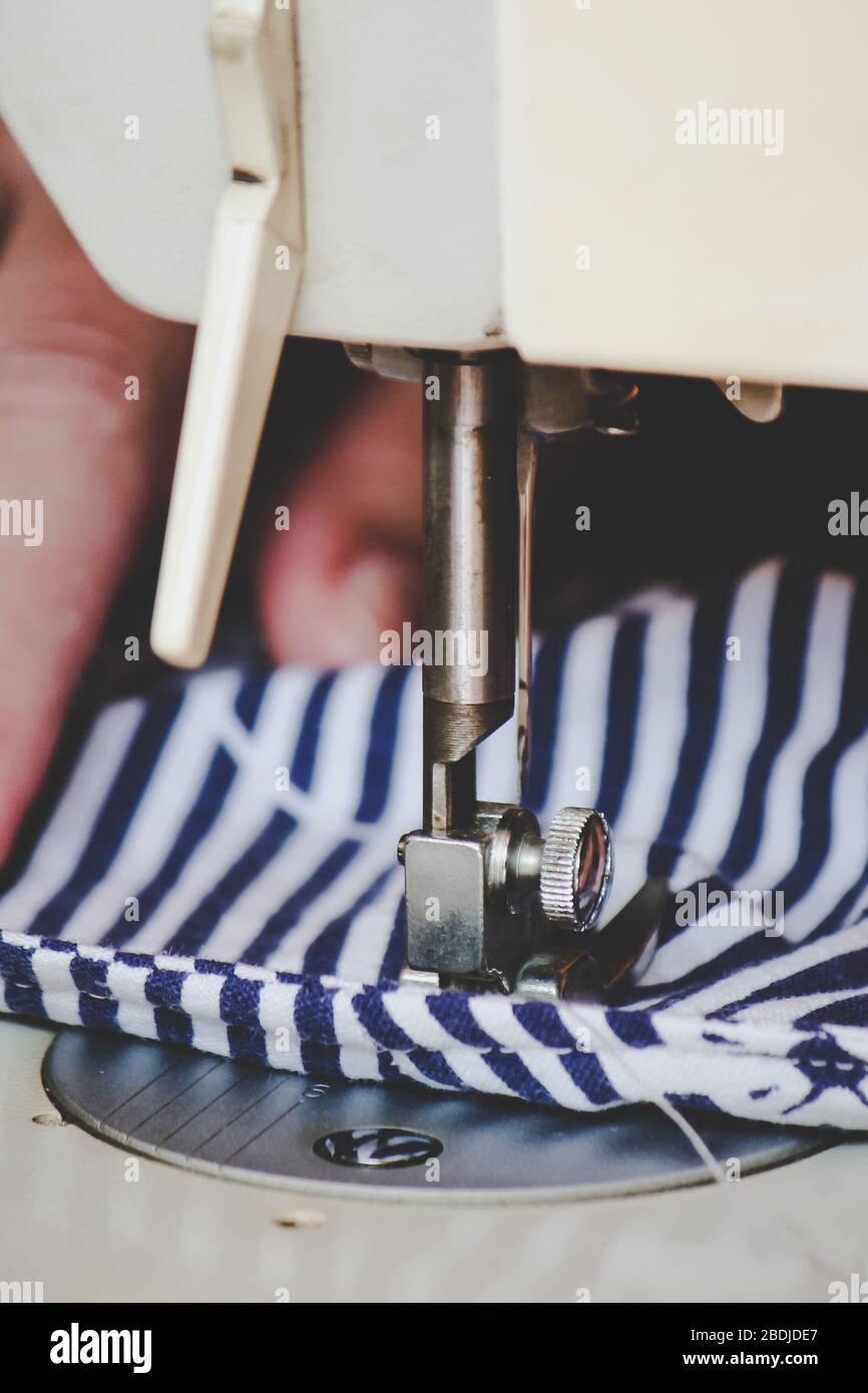 Les mains des femmes utilisant la machine à coudre pour coudre un masque médical coloré du visage pendant la pandémie de coronavirus. Masque de protection fait maison contre le virus. Masques à coudre, COVID-19. Mise au point sélective. Banque D'Images