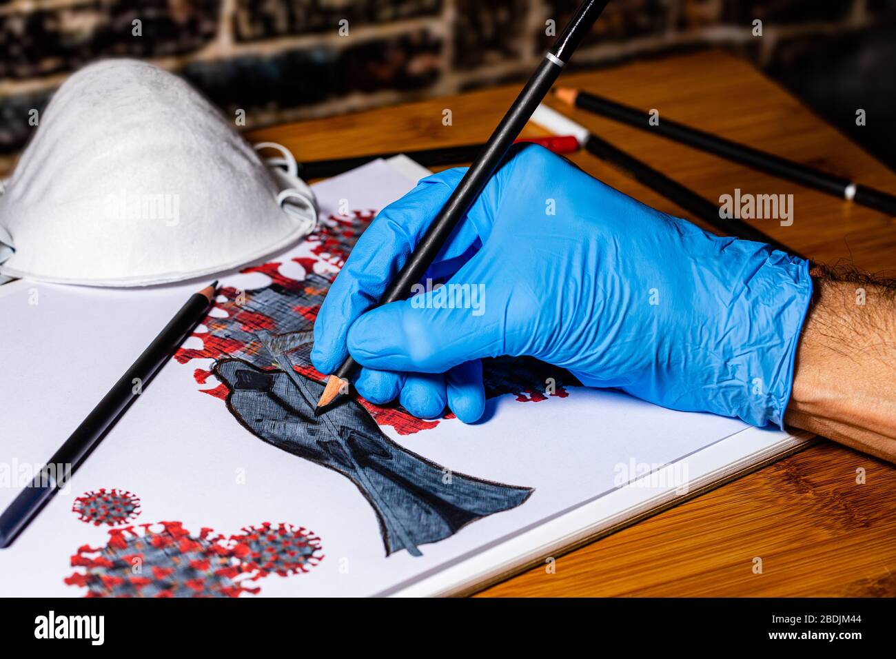 La main d'un artiste caucasien masculin portant un gant médical tout en esquissant différentes copies du Coronavirus avec un masseur centré sur le tirage Banque D'Images