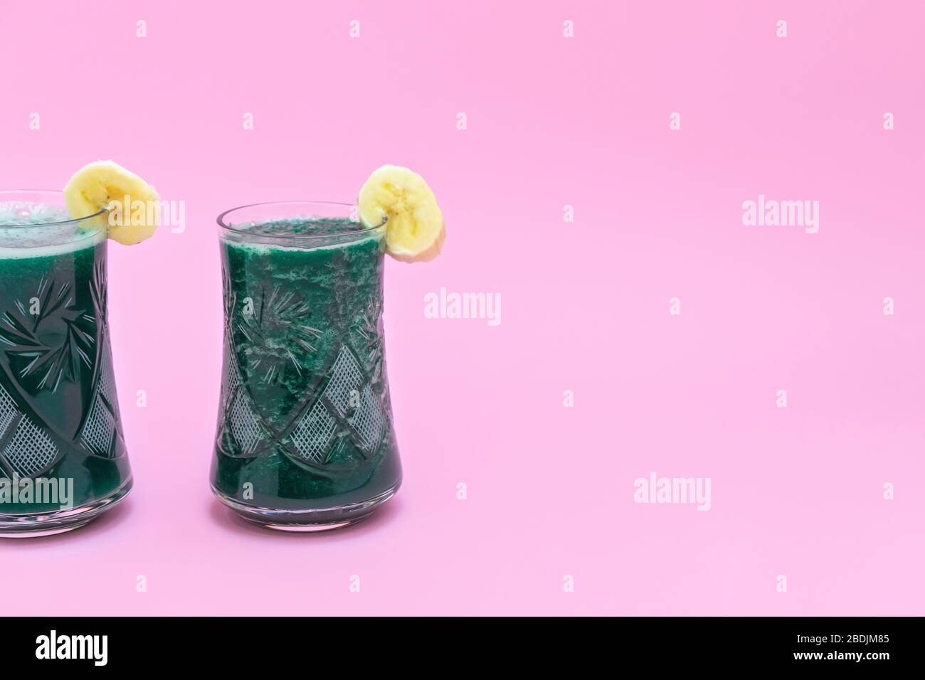 Deux tasses de smoothie detox spiruline avec banane sur fond rose tendre avec espace de copie Banque D'Images