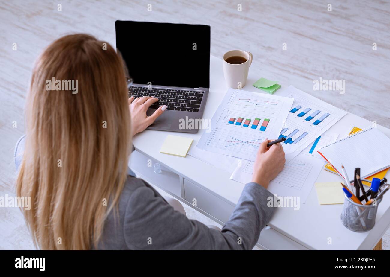 Femme travaille avec des documents, près d'un ordinateur portable avec écran vide Banque D'Images