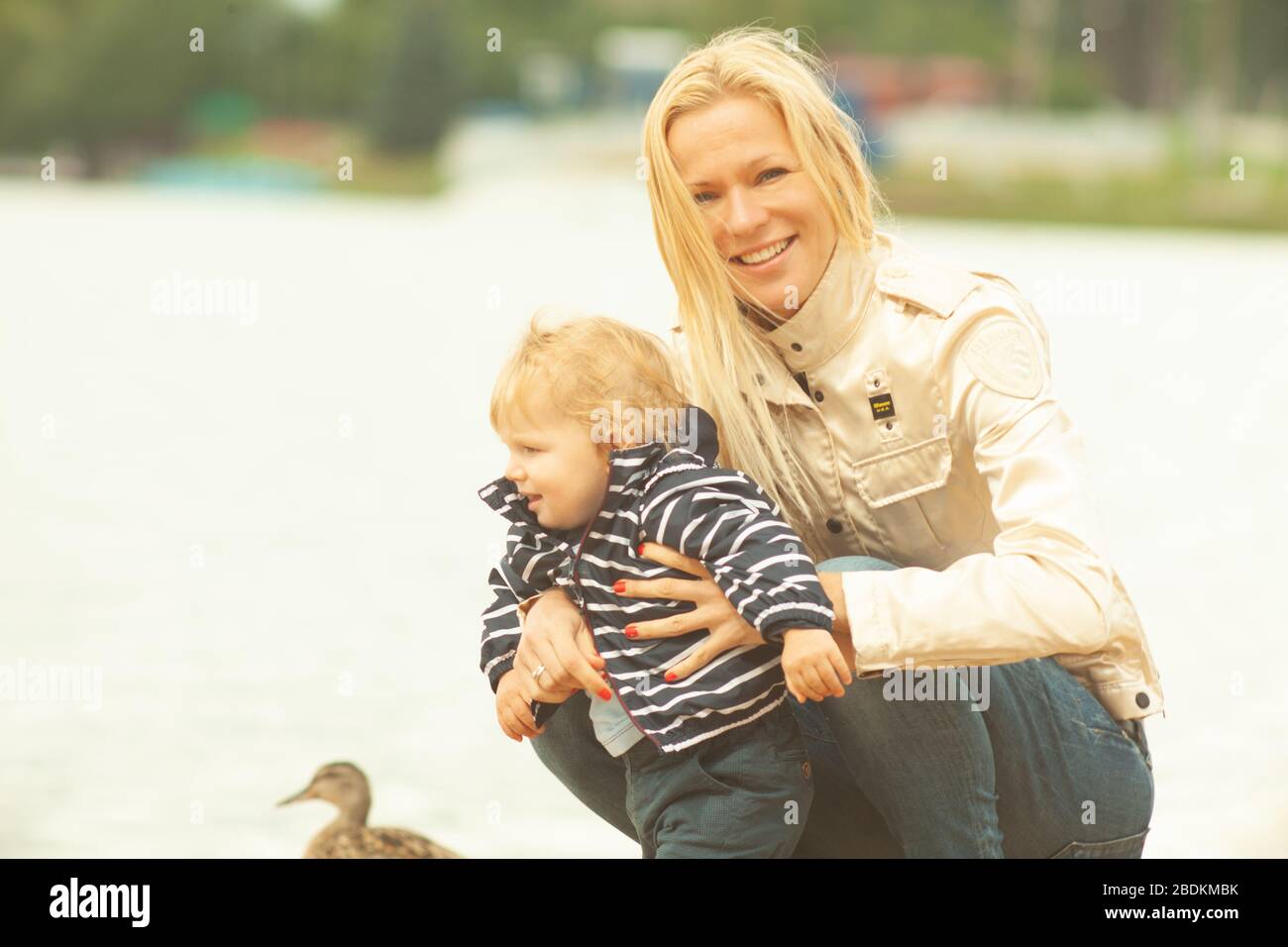 Une mère avec de longs cheveux maintient doucement son petit fils dans ses bras. Photo dans le parc avec lumière naturelle Banque D'Images