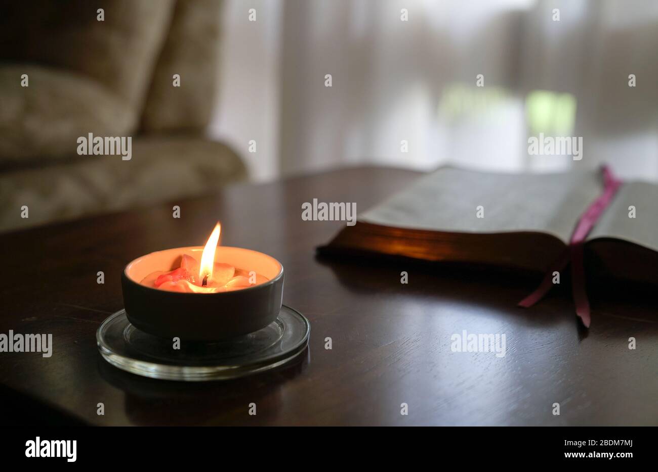 Bougie brûlante sur la table avec livre, rideau et canapé à l'arrière-plan Banque D'Images