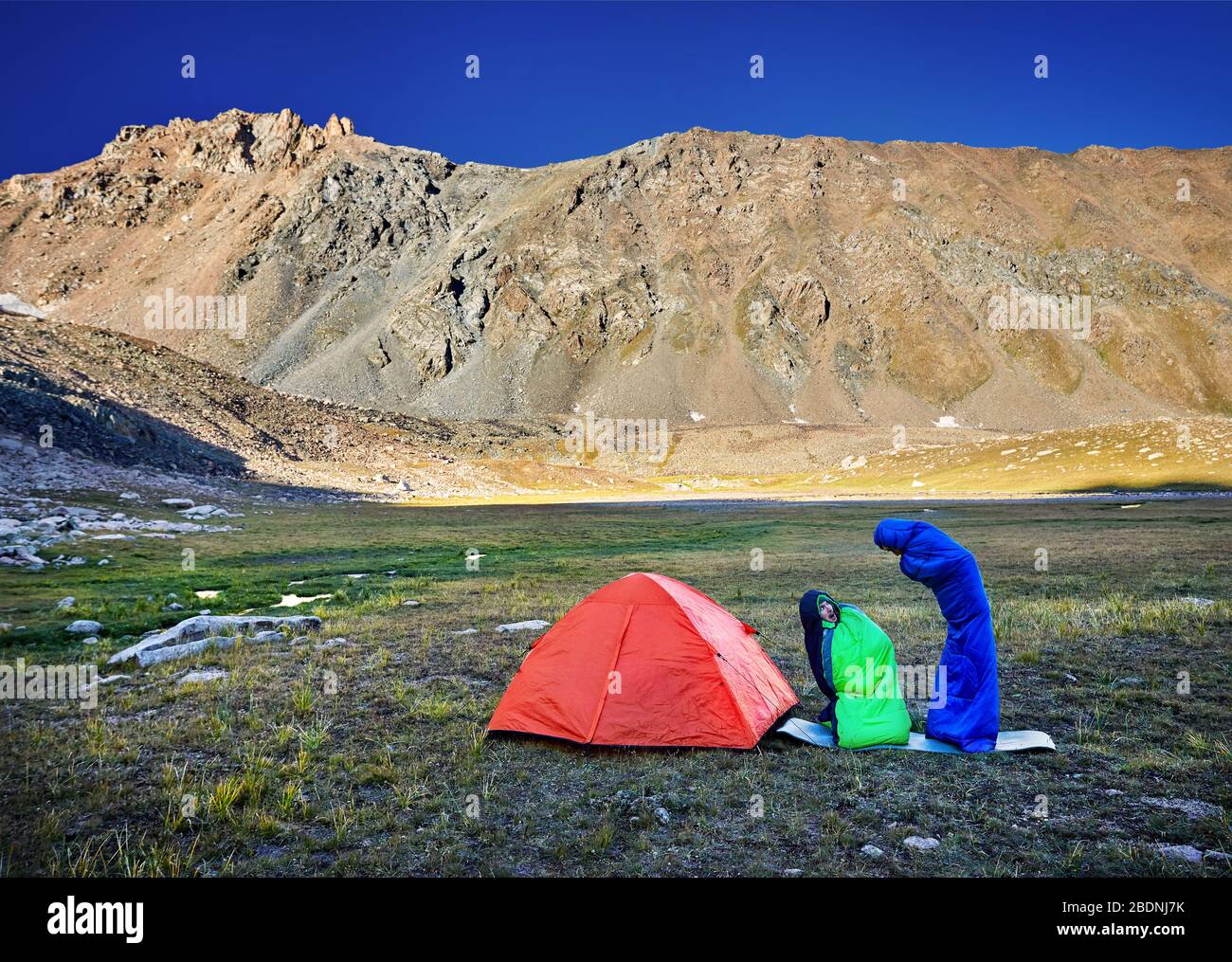 Drôle de détente touristique dans des sacs de couchage près d'orange tente dans les montagnes au lever du soleil Banque D'Images