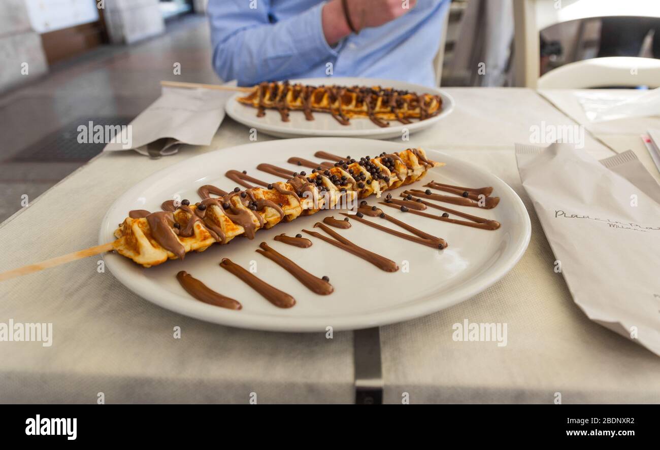 Gaufre sur un bâton avec sauce au chocolat (coulis) , Milan, Italie. Délicieux plats sucrés servis dans une plaque vitrocéramique (restaurant). Banque D'Images